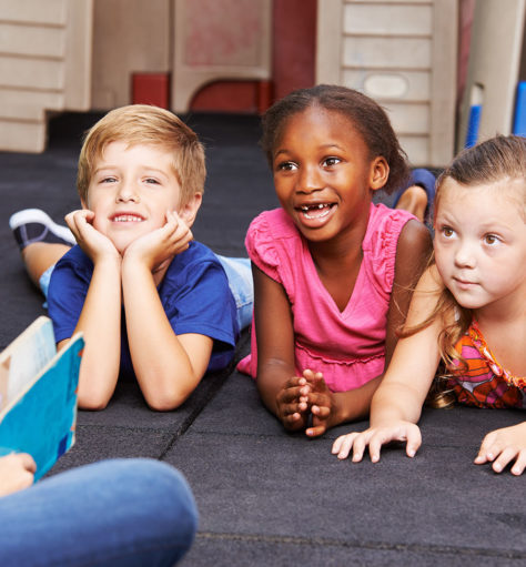 Lachende Kinder im Kindergarten hören beim Vorlesen einer Geschichte zu